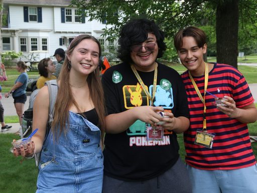 Three students smiling, holding cups of ice cream in the grass.