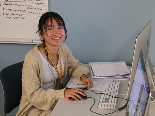 Student smiles at camera infront of computer while doing a project.