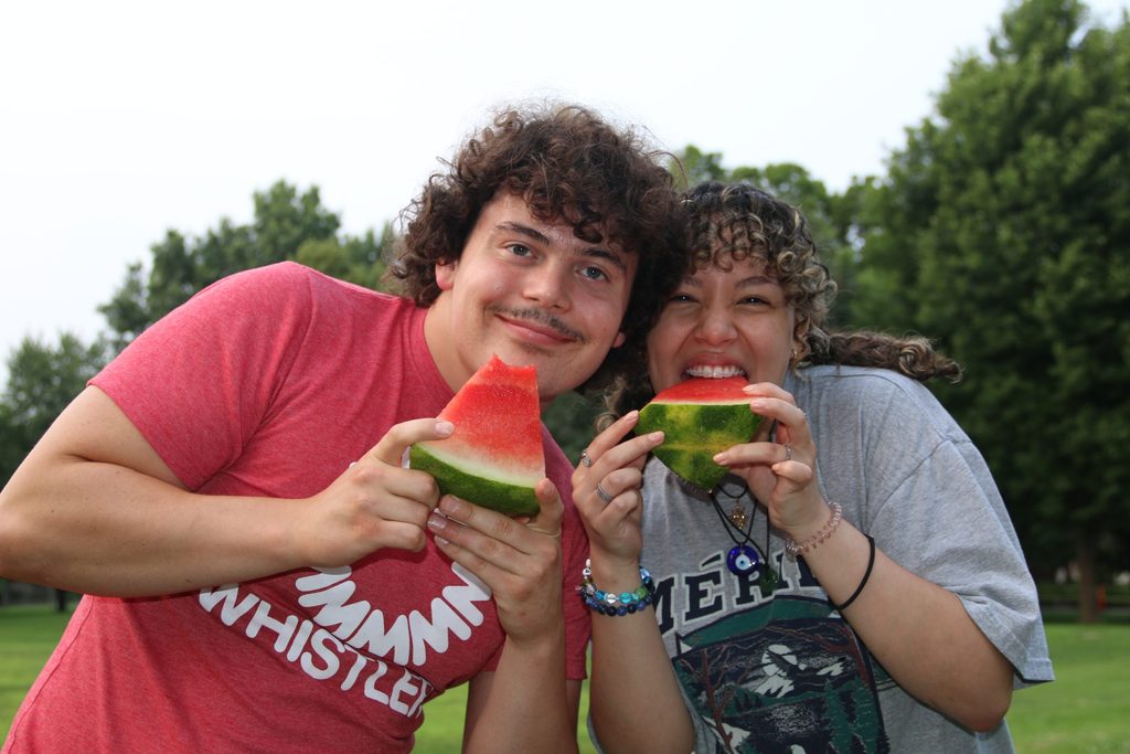 Two program and community assistants smile at the camera while holding watermellon.
