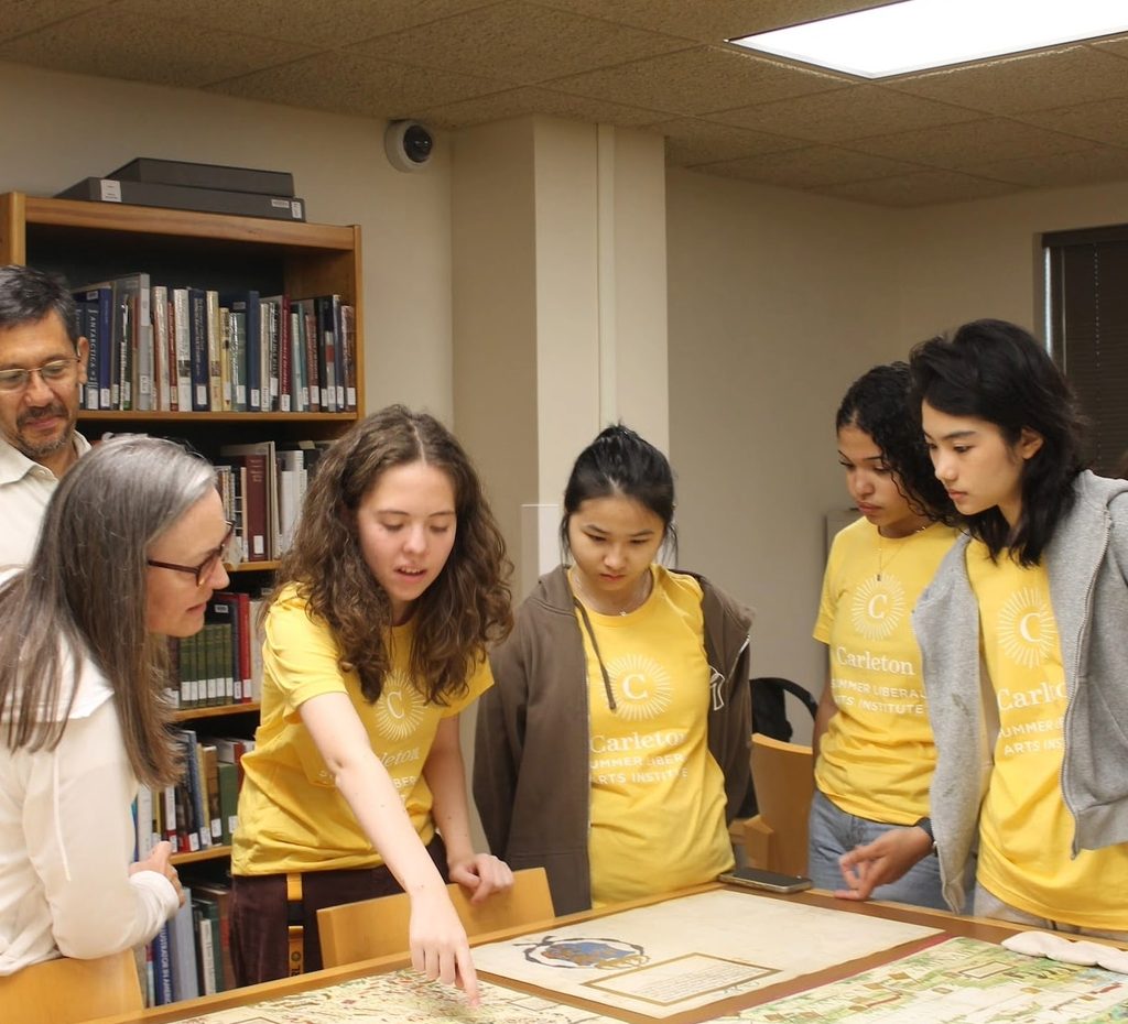 Students gather around a map at the Humanities Symposium with a student pointing and describing something to a parent 