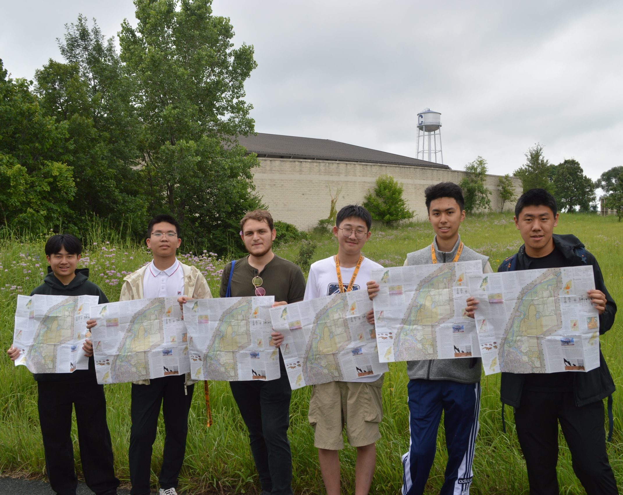 Pre-College students pose in the arb with maps, the Carleton watertower behind them