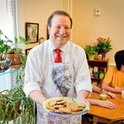 President Poskanzer holds a plate of cookies while wearing an apron emblazoned with the face of Dacie Moses