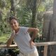 Alicia Telle stands leaning against a wooden railing, green tree fronds in the background