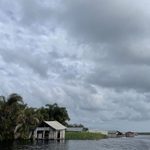 A stilt house sitting by the water, dark clouds hang overhead