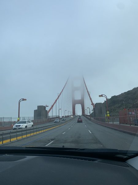 A view of the Golden Gate Bridge from the road of the bridge on a foggy, cloudy day such that the top of the bridge fades off into the fog.