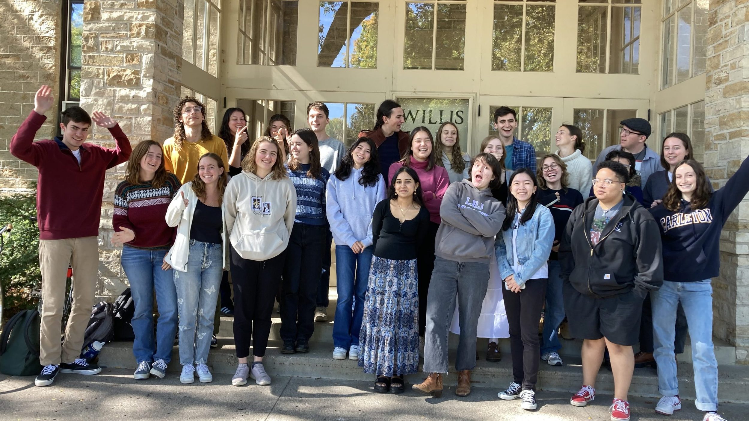Group of Writing Consultants posing playfully in front of Willis Hall on a sunny day.