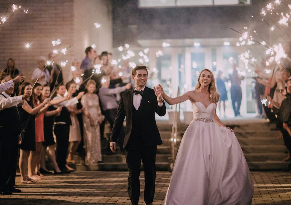 bride and groom walking outdoors as guests surround them with sparklers