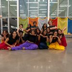 14 student dancers posing posing for a group photo during Diwali 2024, they are wearing bright colored pants with matching black tops