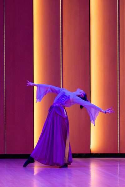 Student in purple flowing dress with arms outstretched to the side and head leaning back