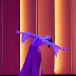 Student in purple flowing dress with arms outstretched to the side and head leaning back