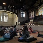 Marc Anderson leading Sound Bath Mediation from the stage, participants seated on the floor below