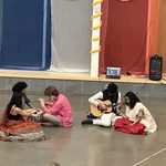 Four students sitting on the floor in Weitz Commons with instruments