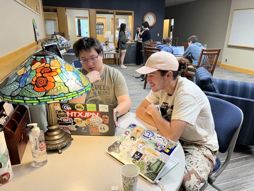 Two students meeting at a round table. A lamp and laptops are on the table.