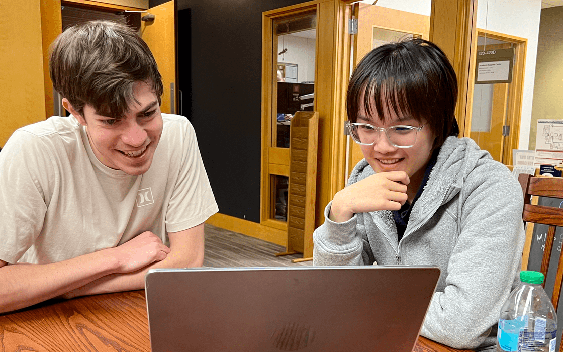 Two students leaning over a laptop in the Writing Center