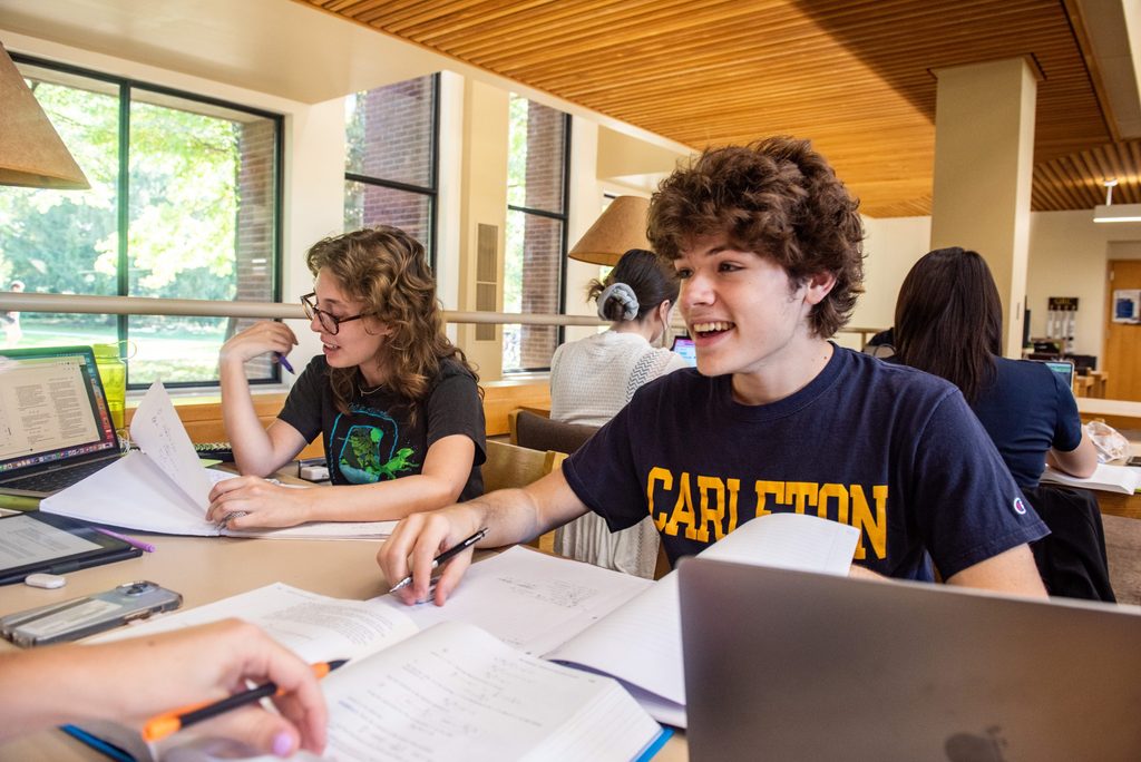 Two students studying at a table with laptops and papers spread out in a brightly lit area of Gould Library