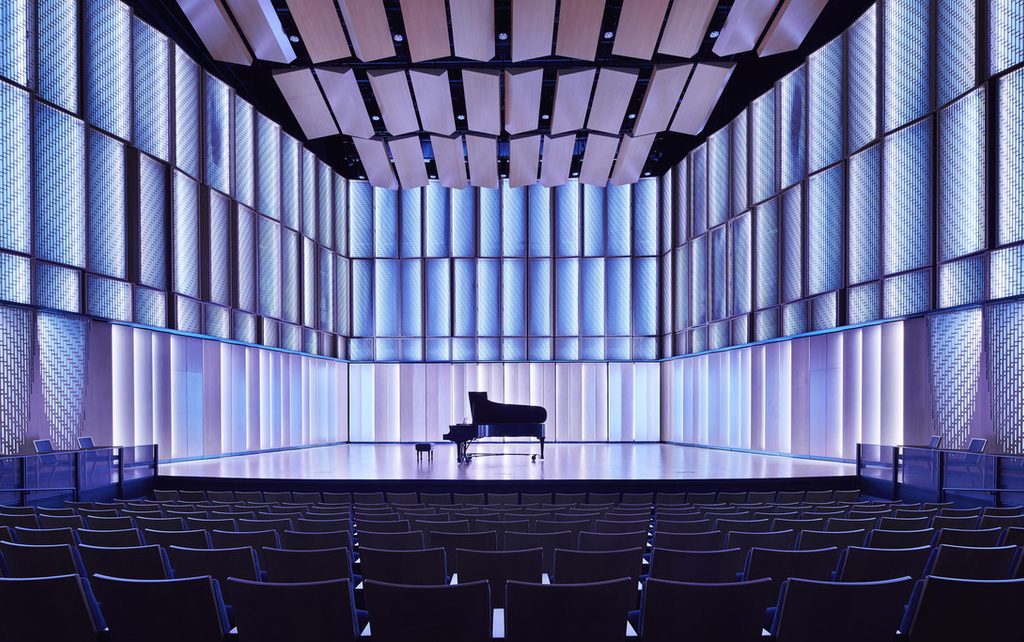 Image of Kracum Performance Hall stage, with piano and blue lighting.