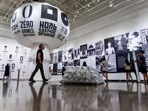 Art exhibit featuring black and white photos, signs, silver missiles, and a white fabric mushroom cloud.