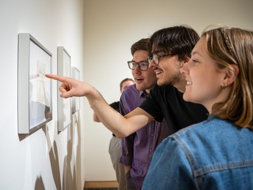 People at an art show smiling at framed art. One person is pointing at the frame.
