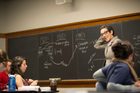 A professor stands at a blackboard in a classroom