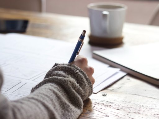 Photo of a hand with a pen writing on a wooden table