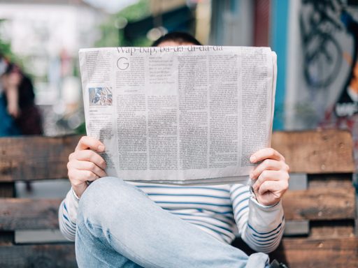 A person holding a newspaper above their face