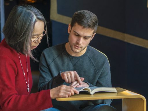 A student and professor look at a book together
