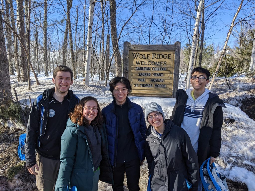 Five students stand in front of the welcome sign for Wolf Ridge Environmental Learning Center.
