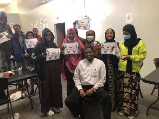 Group of young students and their director holding signs saying Waano.