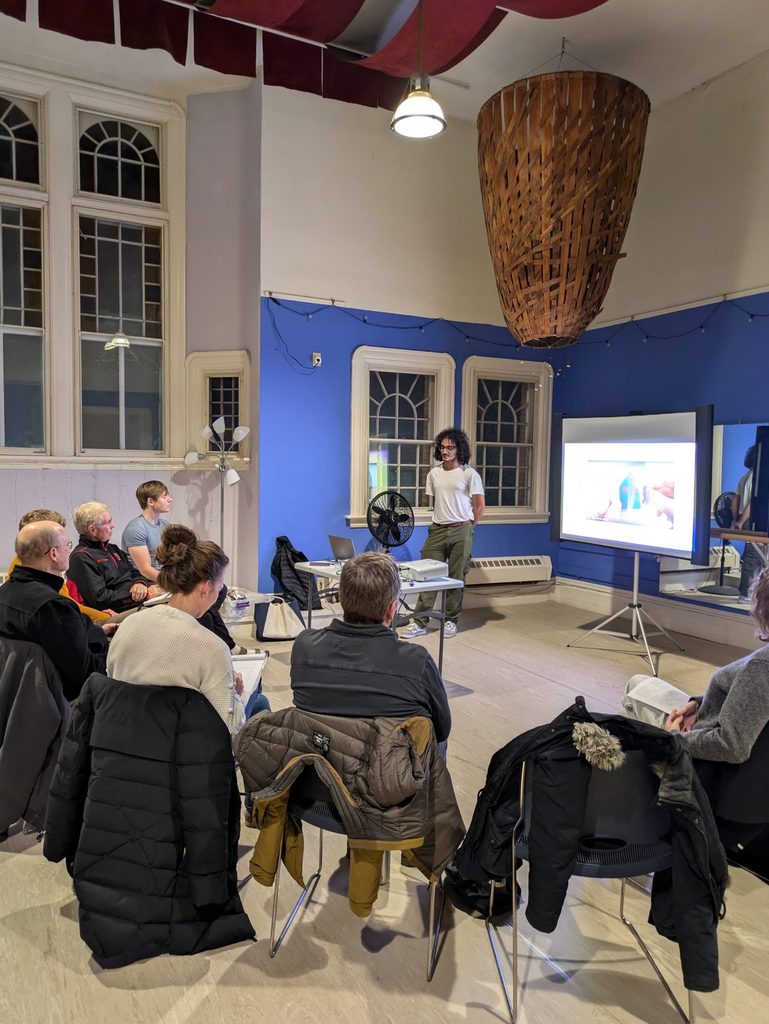 Student presenting an image on a screen to a small seated group of people