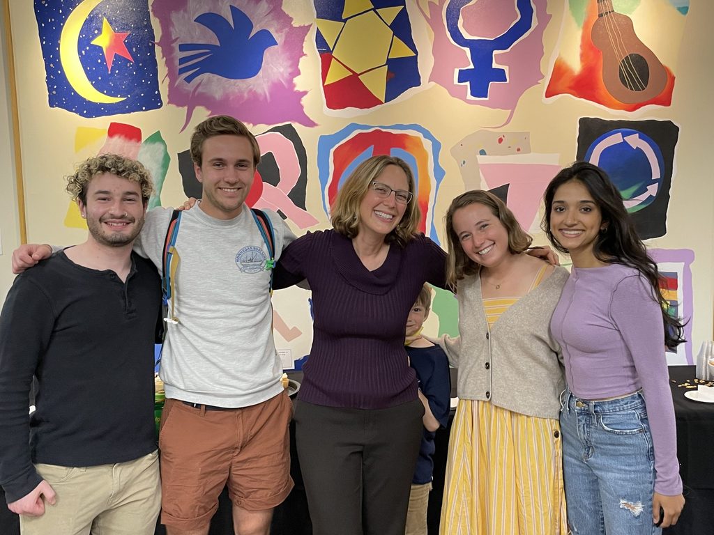 Five people with their arms around each other pose in front of a colorful mural