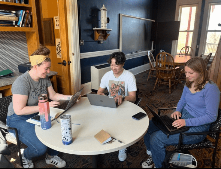 three people gathered at a table with laptops