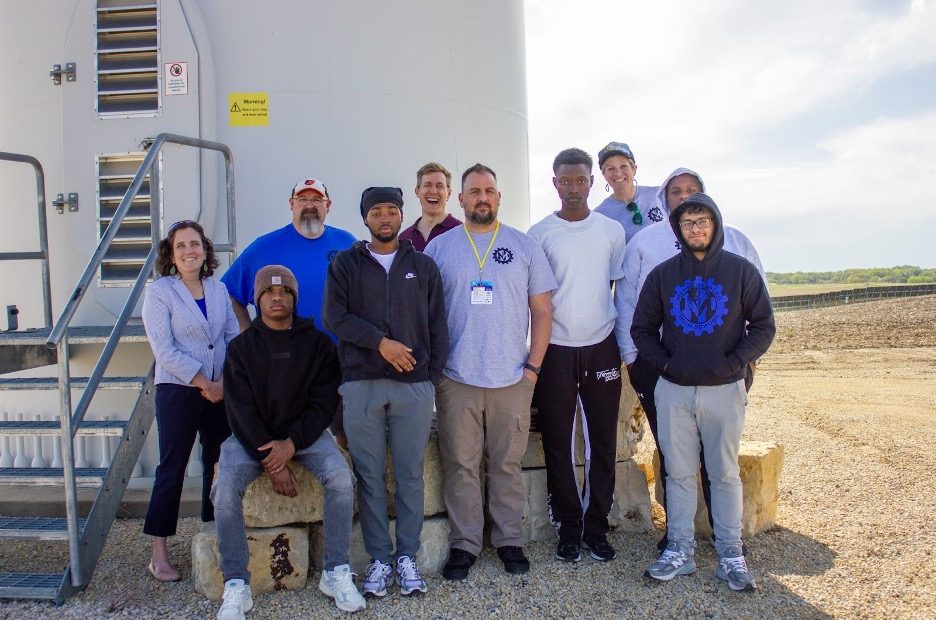 group poses for photo in front of wind turbine