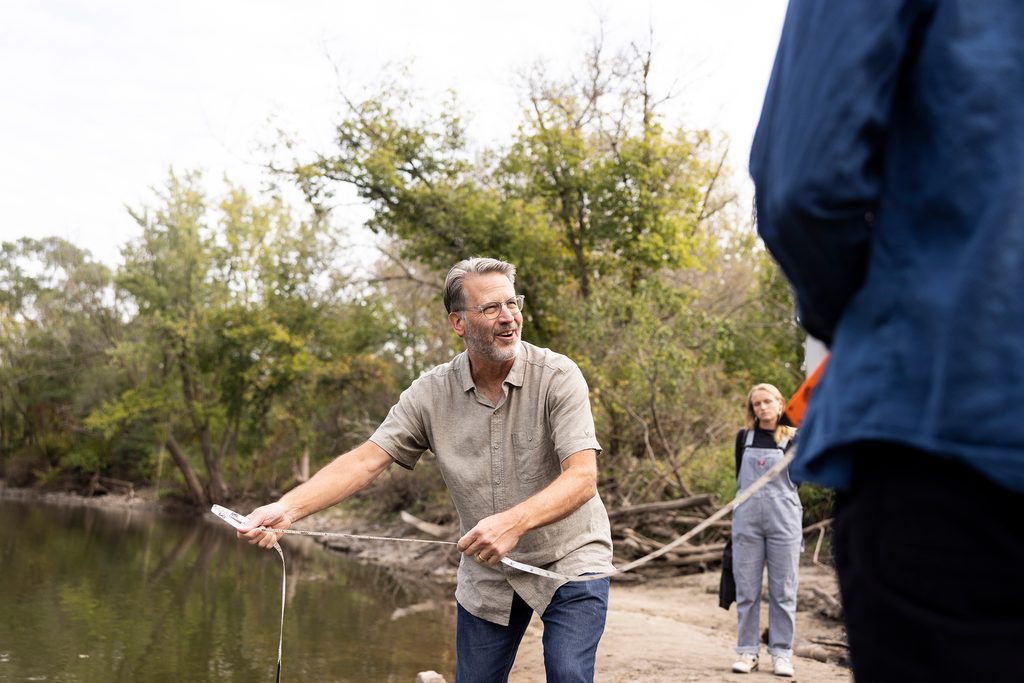 Geology professor Cam Davidson demonstrates how to measure river flow while standing near a river
