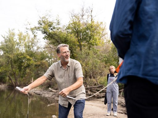 Geology professor Cam Davidson demonstrates how to measure river flow while standing near a river