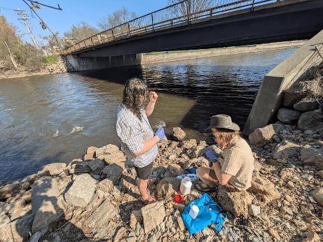two people sampling water on a river bank