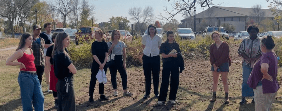 students listening to a lecture outside standing in the grass