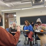 group of students eating pizza in a classroom