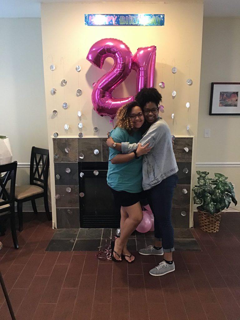 two women hug beneath a 21st birthday banner