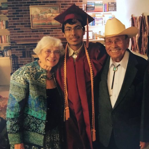 A student in graduation garb with his grandparents