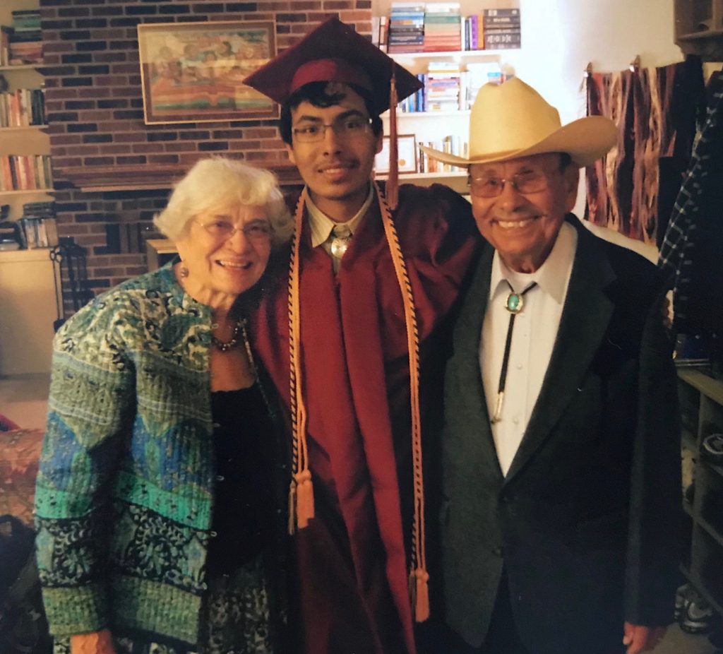 A student in graduation garb with his grandparents