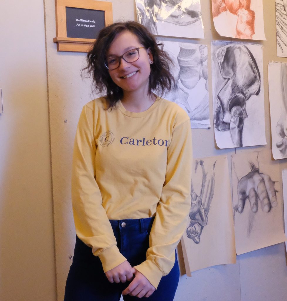 Adela stands in front of a wall of drawings