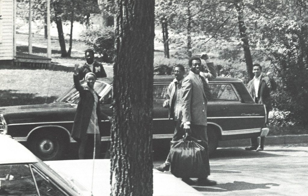 A group of college students stands near a car in the 1960s. 