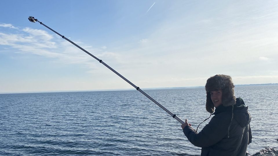Male holds boom pole over lake.