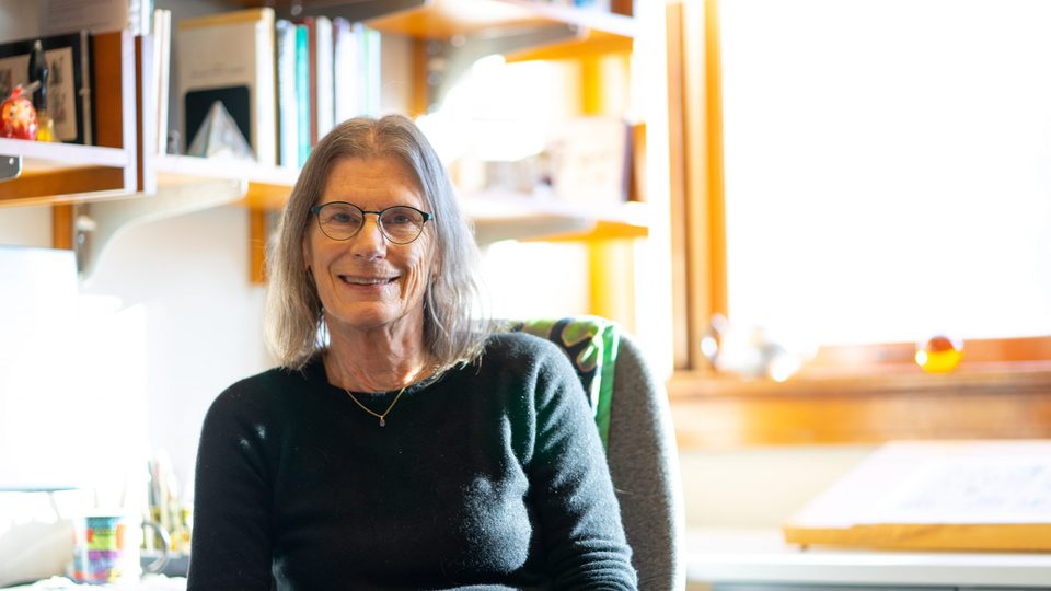 Portrait of a female professor at a desk with books behind her