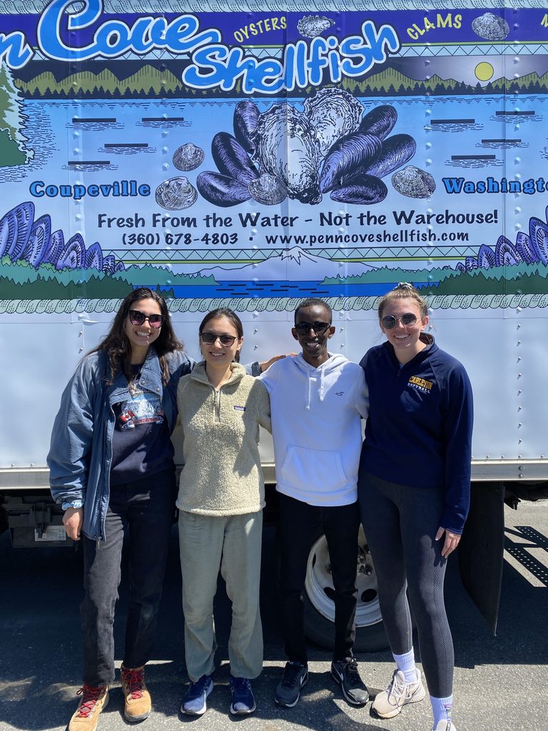 Students pose in front of a "Penn Cove Shellfish" sign.