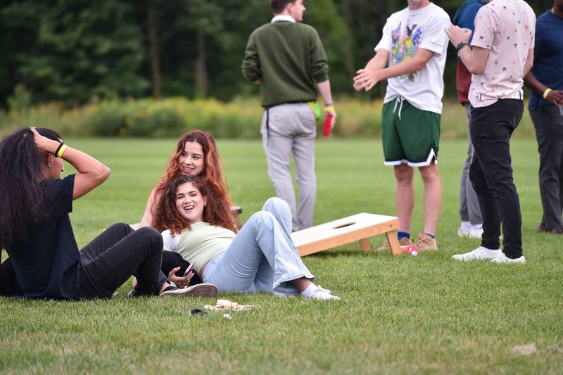Katerina Katakalides '20 relaxes in a friend's lap on the grass in front of some people playing cornhole.