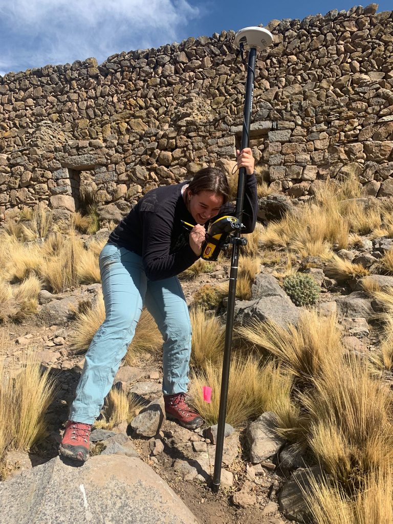 Ezra Kucur ’25 uses a Trimble GPS system amidst tall grasses and rocks.