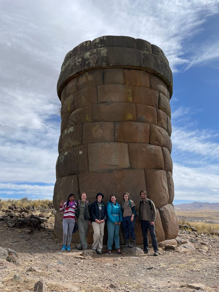Six people pose in front of a chullpa (funerary tower) at Cutimbo in Peru.