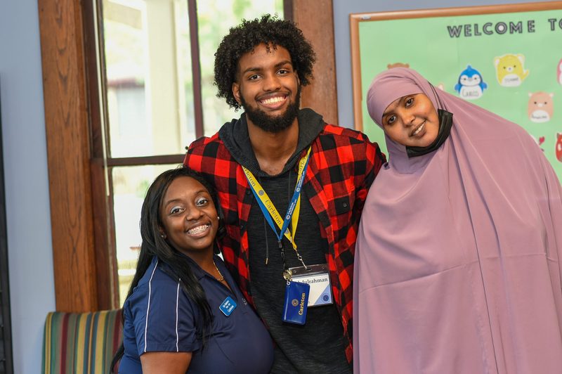 Two students and a staff member smile and lean together for the camera.