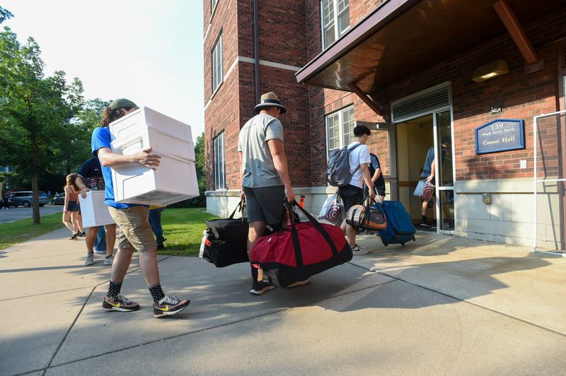 A group of students and family carry multiple suitcases and containers into Cassat.
